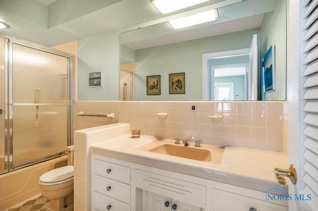 full bathroom with tile walls, vanity, toilet, and bath / shower combo with glass door