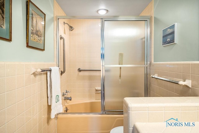 bathroom with toilet, shower / bath combination with glass door, tile walls, and a wainscoted wall