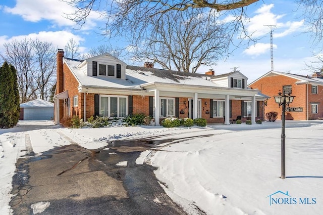 view of front of house with covered porch, brick siding, a detached garage, an outdoor structure, and a chimney