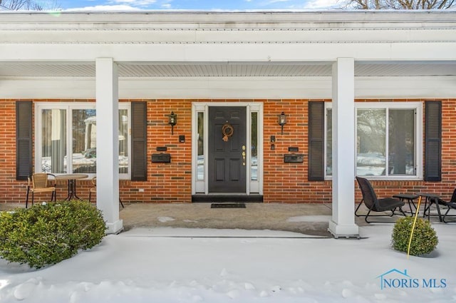 snow covered property entrance featuring brick siding and a porch