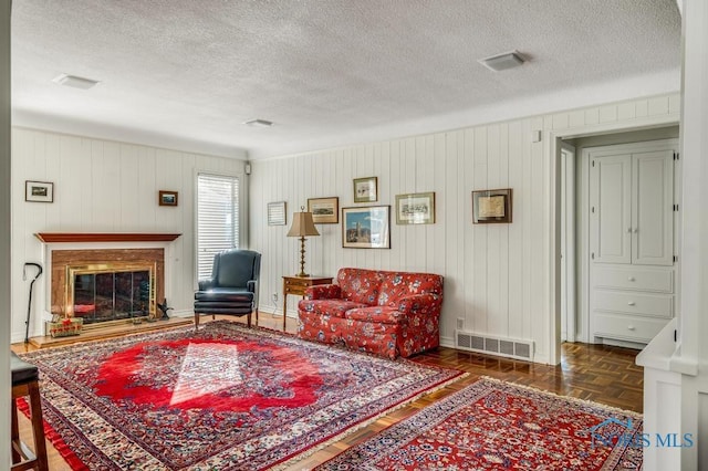 living room with a textured ceiling, a glass covered fireplace, visible vents, and baseboards