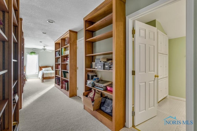 hall with a textured ceiling, baseboards, and light colored carpet