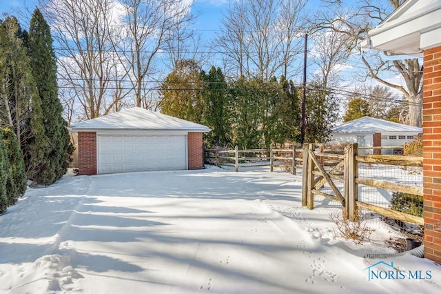 snowy yard with a garage, an outdoor structure, and fence