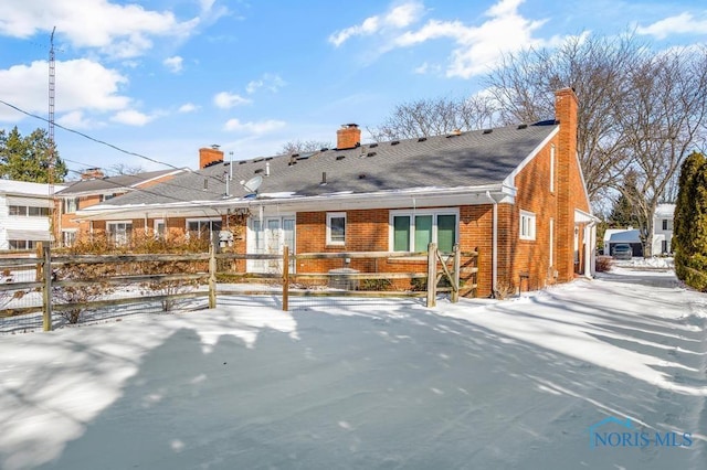 snow covered rear of property featuring brick siding, a chimney, and fence