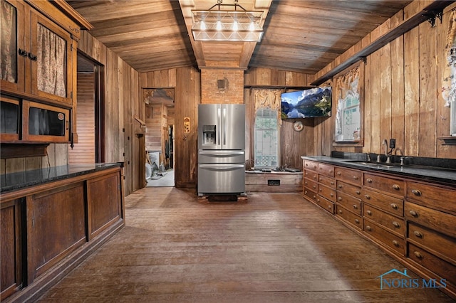 kitchen with stainless steel fridge, dark countertops, wooden ceiling, wood walls, and a sink
