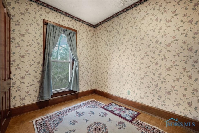 spare room with wallpapered walls and baseboards