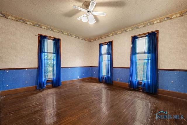 empty room with wainscoting, wood-type flooring, and wallpapered walls
