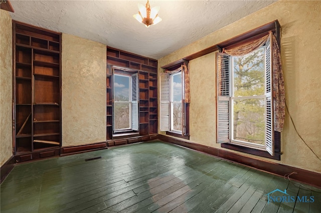 spare room featuring a textured ceiling, a textured wall, hardwood / wood-style floors, and a healthy amount of sunlight