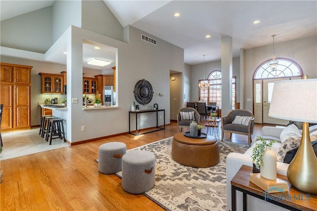 living room with high vaulted ceiling, light wood-style flooring, visible vents, and a notable chandelier