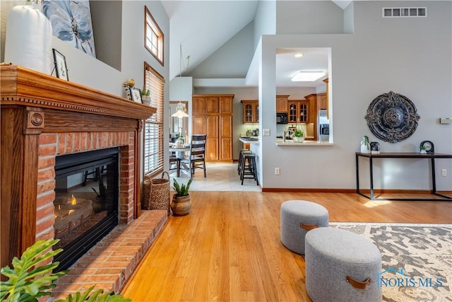 living area featuring high vaulted ceiling, a fireplace, visible vents, baseboards, and light wood finished floors