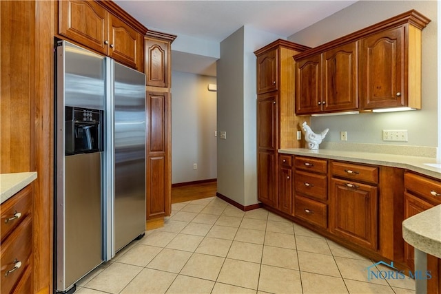 kitchen featuring light tile patterned floors, light countertops, brown cabinets, and stainless steel fridge with ice dispenser