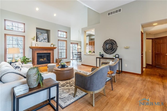 living room with a wealth of natural light, light wood finished floors, a brick fireplace, and visible vents