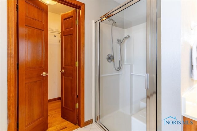 full bath featuring wood finished floors, a closet, a shower stall, and baseboards