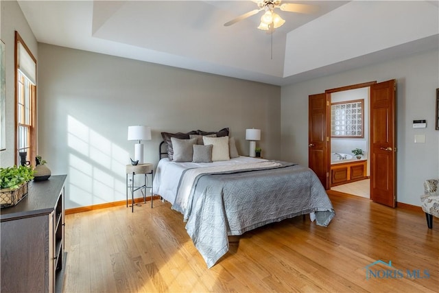 bedroom featuring lofted ceiling, light wood-style flooring, a ceiling fan, baseboards, and a tray ceiling