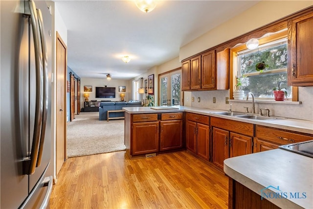 kitchen with brown cabinets, light countertops, freestanding refrigerator, open floor plan, and a sink