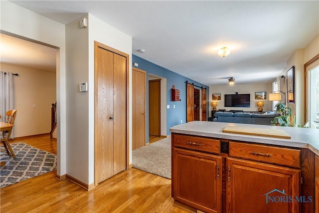 kitchen with a barn door, light wood-style floors, open floor plan, light countertops, and brown cabinetry