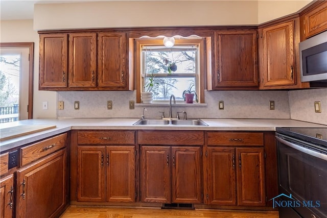 kitchen featuring brown cabinets, light countertops, stainless steel microwave, electric range, and a sink