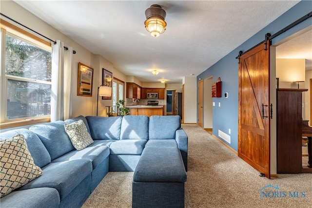 living room with baseboards, a barn door, light colored carpet, and a healthy amount of sunlight