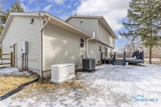 snow covered house featuring fence, a deck, and central air condition unit