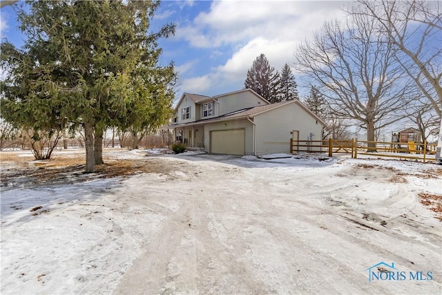 view of snowy exterior with a garage, driveway, and fence