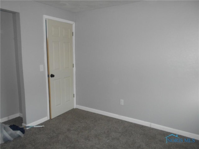 unfurnished room featuring baseboards and dark colored carpet