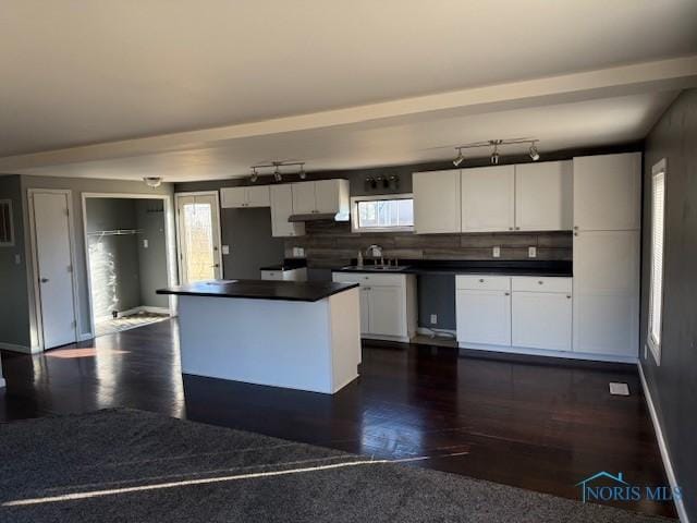 kitchen featuring a sink, white cabinets, backsplash, dark countertops, and dark wood finished floors