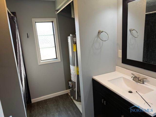 bathroom with gas water heater, curtained shower, vanity, wood finished floors, and baseboards