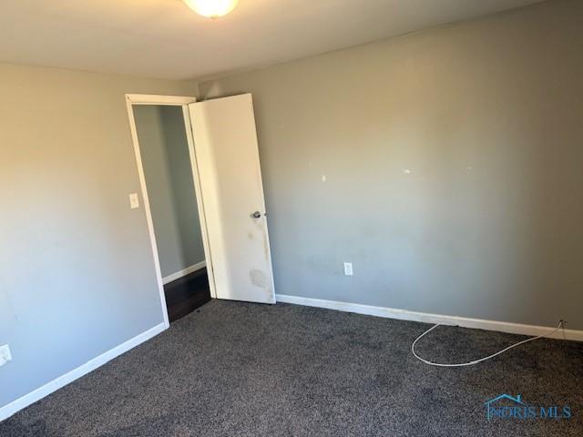 spare room with baseboards and dark carpet