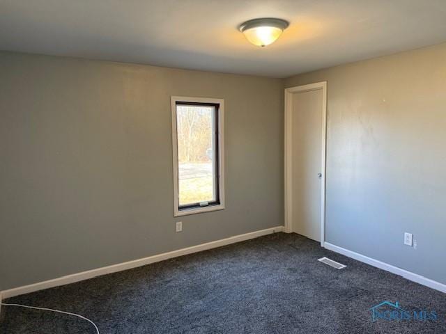 spare room featuring visible vents, dark carpet, and baseboards