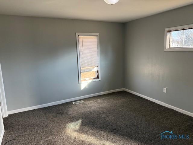 unfurnished room featuring baseboards, visible vents, and dark colored carpet