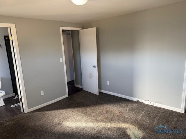 unfurnished bedroom featuring a closet, dark carpet, and baseboards