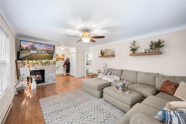 living room featuring a healthy amount of sunlight, a baseboard radiator, wood-type flooring, and a stone fireplace