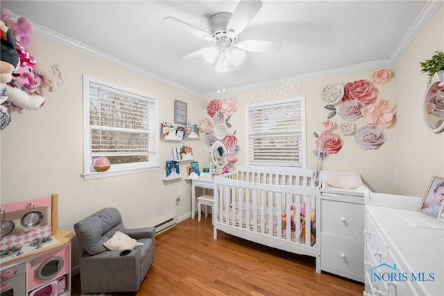 bedroom featuring a crib, multiple windows, light wood-type flooring, and a baseboard radiator