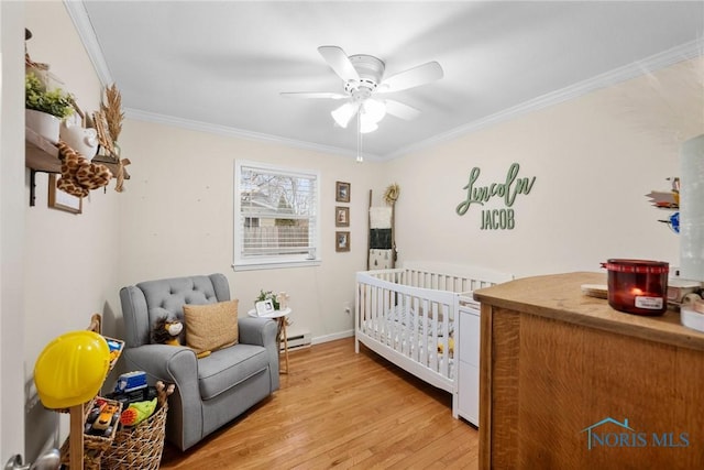 bedroom with baseboard heating, ornamental molding, light wood-style floors, a ceiling fan, and a nursery area