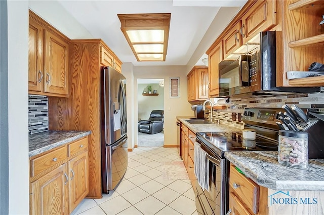 kitchen with light tile patterned floors, baseboards, appliances with stainless steel finishes, a sink, and backsplash