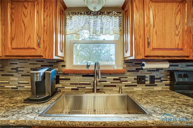 kitchen featuring tasteful backsplash, brown cabinetry, a sink, and stone counters