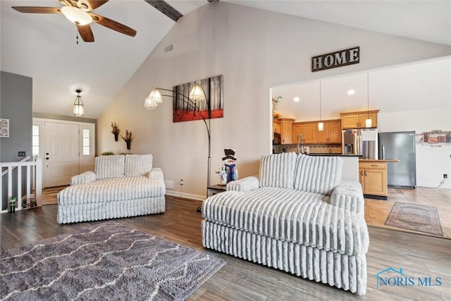 living area featuring baseboards, visible vents, a ceiling fan, light wood-type flooring, and high vaulted ceiling