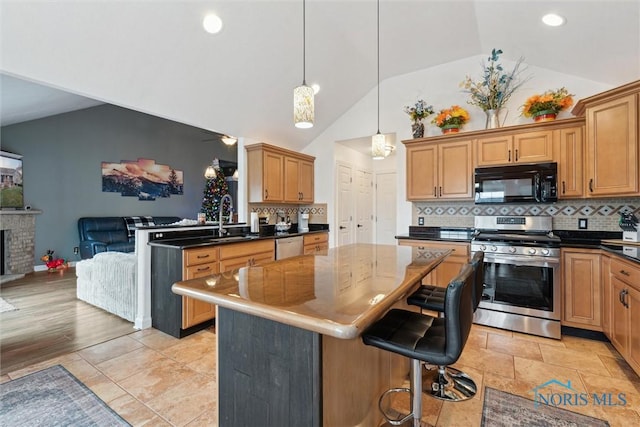 kitchen with stainless steel range with gas cooktop, dark countertops, a sink, black microwave, and a kitchen breakfast bar