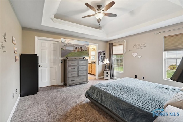 bedroom with ceiling fan, light carpet, baseboards, a raised ceiling, and ensuite bath