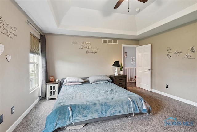 carpeted bedroom with baseboards, visible vents, a raised ceiling, and a ceiling fan