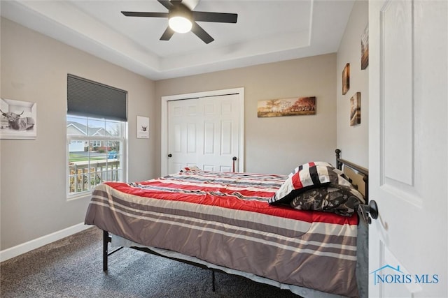 carpeted bedroom with a tray ceiling, a ceiling fan, and baseboards