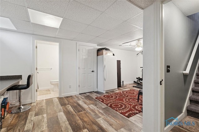 interior space with a ceiling fan, wood finished floors, a paneled ceiling, and baseboards