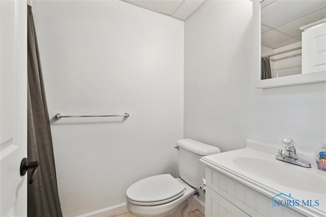 bathroom featuring a paneled ceiling, curtained shower, toilet, vanity, and baseboards