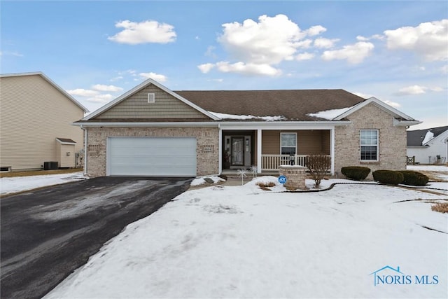 ranch-style house featuring an attached garage, covered porch, aphalt driveway, and brick siding