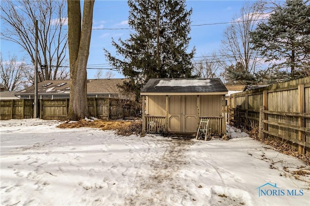 snowy yard featuring a storage shed, an outdoor structure, and a fenced backyard