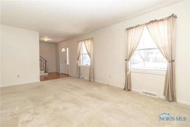 unfurnished room with baseboards, stairway, visible vents, and light colored carpet