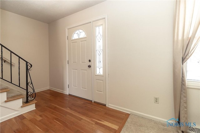 foyer entrance with stairway, wood finished floors, and baseboards