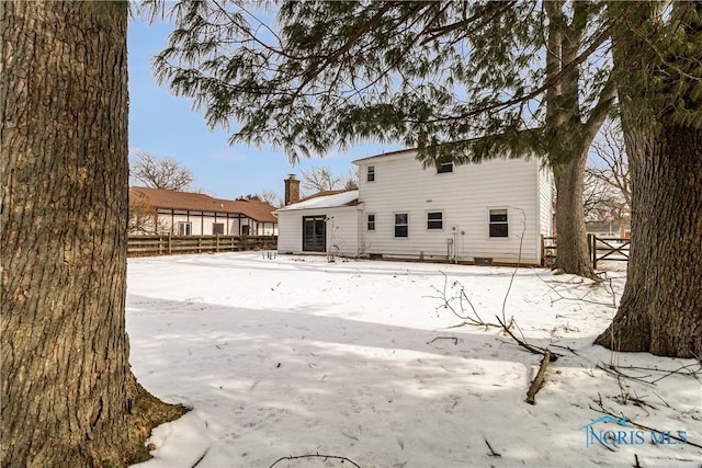 snow covered back of property with a chimney and fence