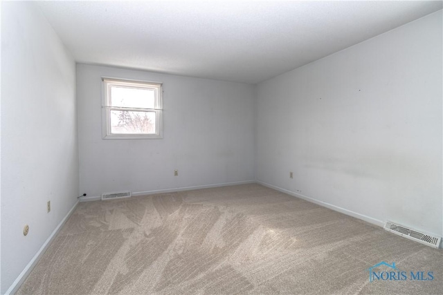 spare room with light colored carpet, visible vents, and baseboards