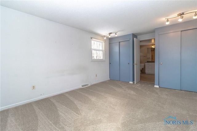 unfurnished bedroom with baseboards, carpet, visible vents, and two closets